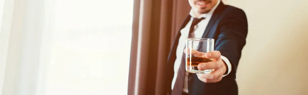 Vista recortada del hombre de negocios en ropa formal sosteniendo vaso de whisky en la habitación de hotel — Stock Photo