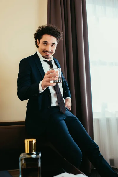 Alegre hombre de negocios en ropa formal sosteniendo vaso de whisky en la habitación de hotel - foto de stock