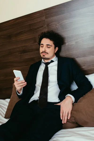 Homme d'affaires utilisant smartphone sur le lit dans la chambre d'hôtel — Photo de stock