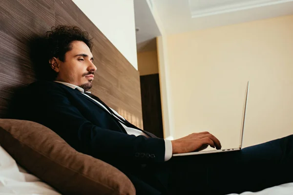 Homem de negócios em terno teletrabalho no laptop no quarto de hotel — Fotografia de Stock