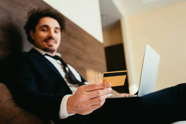 Foco seletivo de feliz empresário compras on-line com cartão de crédito e laptop no quarto de hotel — Fotografia de Stock