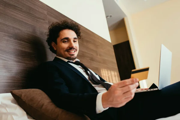 Fröhlicher Geschäftsmann kauft online mit Kreditkarte und Laptop im Hotelzimmer ein — Stockfoto