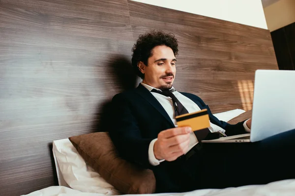 Handsome businessman shopping online with credit card and laptop in hotel room — Stock Photo