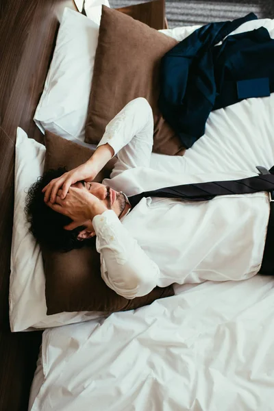 Вид сверху на уставшего бизнесмена, отдыхающего на кровати в номере отеля — стоковое фото