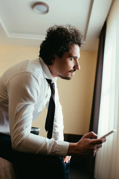 Uomo d'affari pensieroso in abbigliamento formale utilizzando smartphone in camera d'albergo — Foto stock