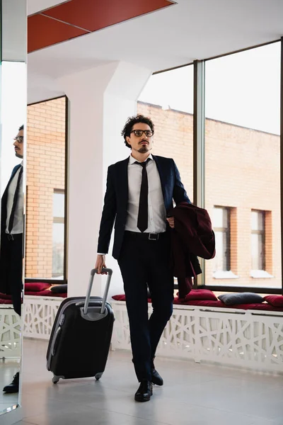 Uomo d'affari in tuta che cammina nella hall dell'hotel con borsa da viaggio — Foto stock