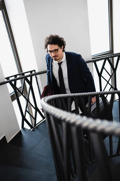 Избирательный фокус бизнесмена с чемоданом, поднимающимся по лестнице в отеле — стоковое фото