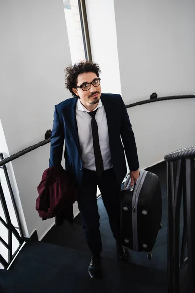 Businessman holding travel bag and going up on stairs in hotel — Stock Photo