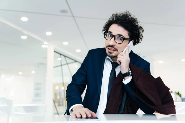 Handsome businessman with passport talking on smartphone while making check-in at the hotel — Stock Photo