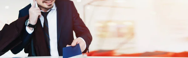 Vista cortada de homem de negócios com passaporte falando no smartphone enquanto faz o check-in no hotel — Fotografia de Stock