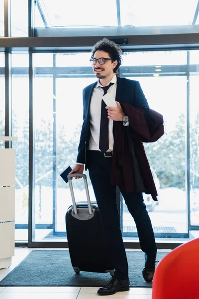 Sonriente hombre de negocios con smartphone, pasaporte y bolsa de viaje en el hall del hotel - foto de stock