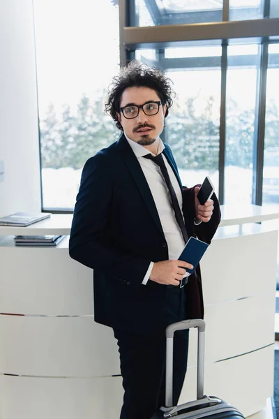 Businessman with smartphone, passport and baggage waiting for check-in at the hotel — Stock Photo