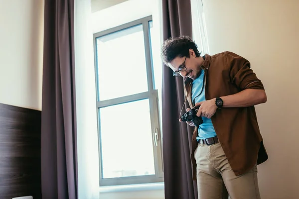 Усміхнений чоловік в окулярах дивиться на фотоапарат біля вікна в готельному номері — стокове фото