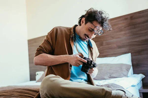 Fotógrafo en anteojos mirando cámara fotográfica en habitación de hotel - foto de stock