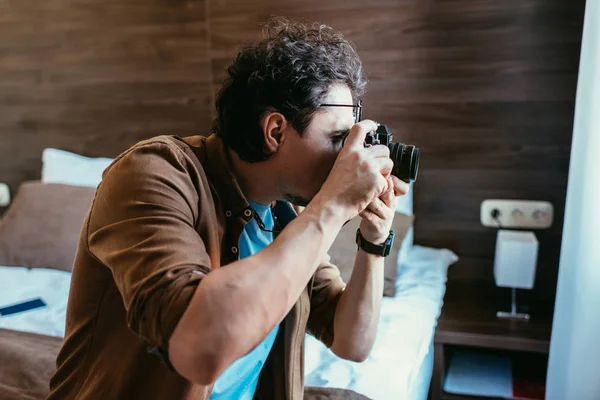 Photographe homme adulte en lunettes prenant des photos à la caméra dans la chambre d'hôtel — Photo de stock