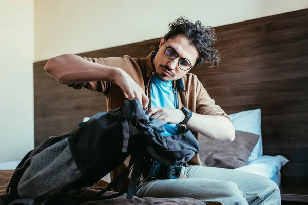 Turista masculino tomando algo de la mochila en la habitación de hotel - foto de stock