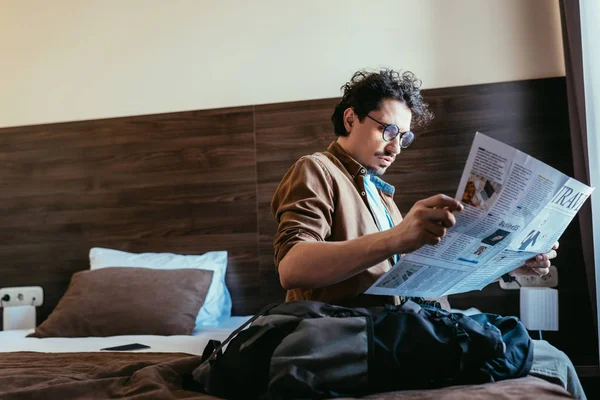 Man reading travel newspaper and sitting on bed in hotel room — Stock Photo