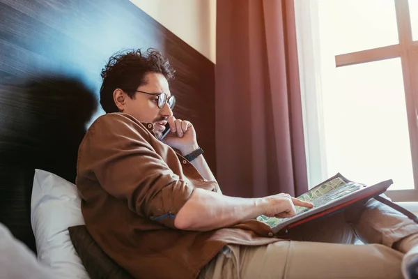 Turista hablando en smartphone mientras mira el mapa en la habitación del hotel - foto de stock