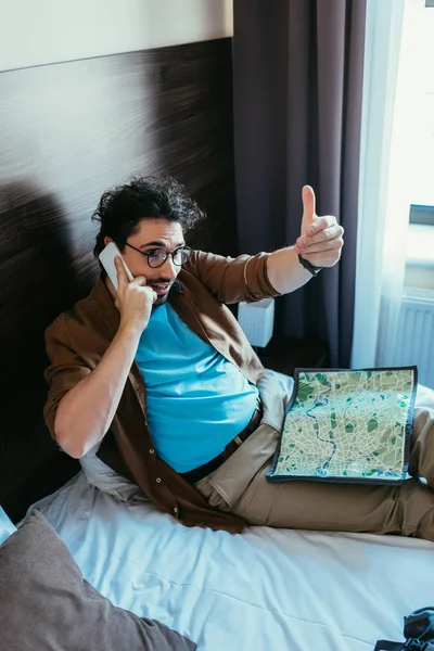 Touriste masculin avec carte parlant sur smartphone et geste dans la chambre d'hôtel — Photo de stock