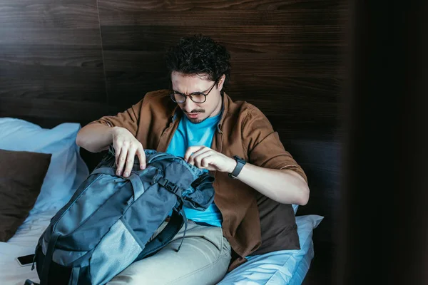 Turista masculino mirando en la mochila en la habitación de hotel - foto de stock