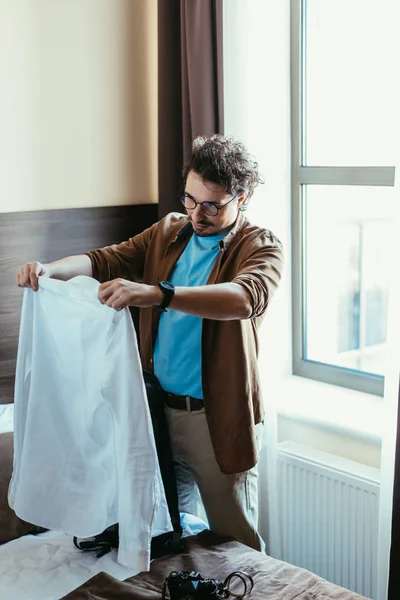 Guapo macho turista poner camisa en mochila en hotel habitación - foto de stock