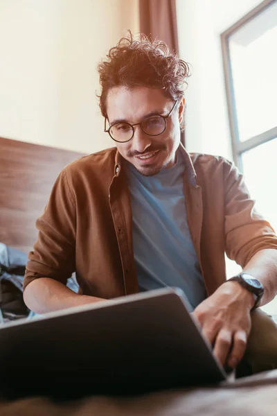 Selective focus of happy man using laptop in hotel room with sunlight — Stock Photo