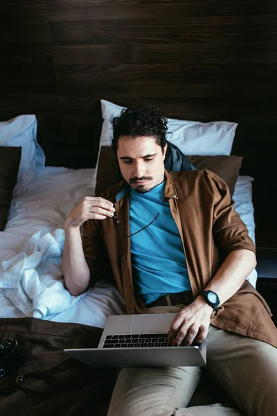 Viajero masculino con anteojos usando laptop en habitación de hotel - foto de stock