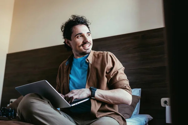 Sourire photographe masculin en utilisant un ordinateur portable dans la chambre d'hôtel — Photo de stock