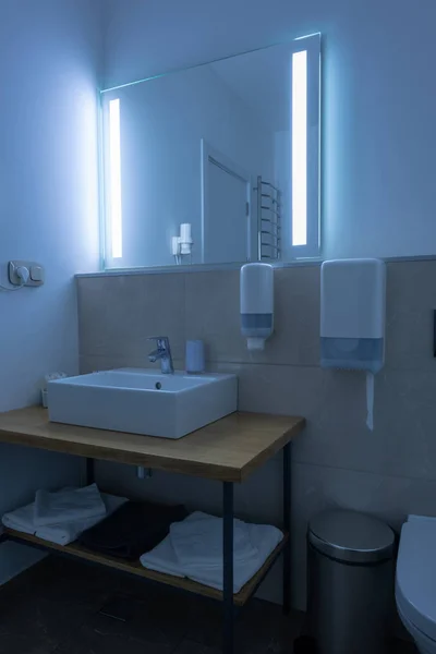 Hotel bathroom with washstand and towels with neon light on mirror — Stock Photo
