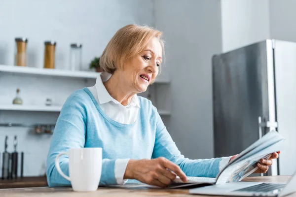 Senior femme assis et lire le journal dans la cuisine — Photo de stock