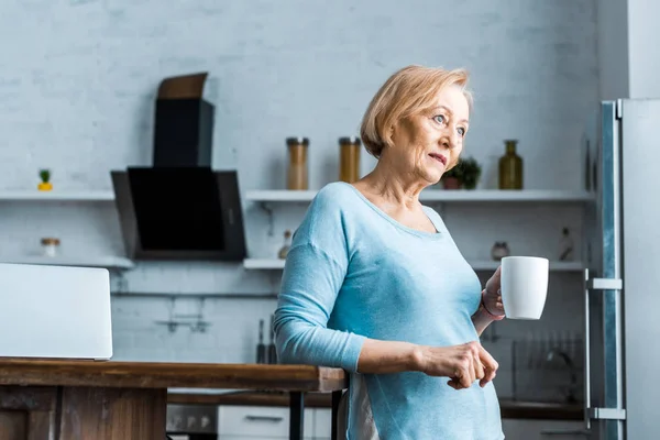 Senior woman with cup of coffee looking away in kitchen with copy space — Stock Photo