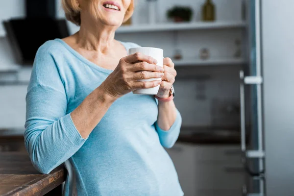 Cropped view of smiling senior woman holding cup of coffee at home with copy space — Stock Photo