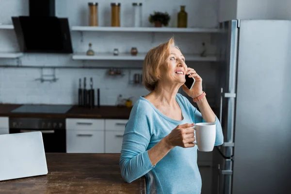 Femme âgée souriante avec tasse de café parler sur smartphone à la maison avec espace de copie — Photo de stock
