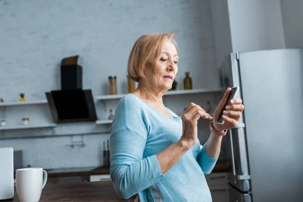 Seniorin nutzt Smartphone in Küche mit Kopierraum — Stockfoto