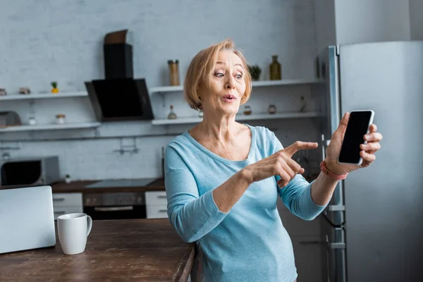 Donna anziana sorpresa che punta con il dito contro lo smartphone a casa — Foto stock