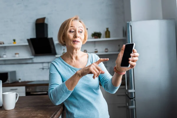 Donna anziana sorpresa che punta con il dito contro lo smartphone a casa — Foto stock