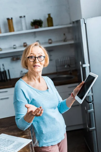 Seniorin mit Brille bedient digitales Tablet und gestikuliert in Küche mit der Hand — Stockfoto