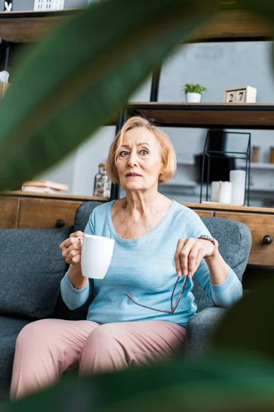 Вибірковий фокус старшої жінки, сидячи на дивані з чашкою кави у вітальні — стокове фото