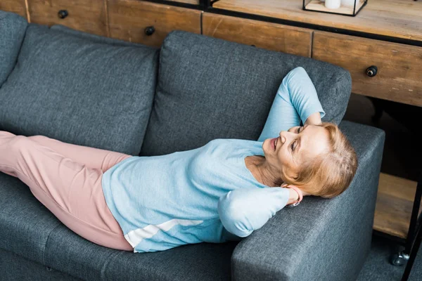 Smiling senior woman with hands on head lying and resting on couch — Stock Photo