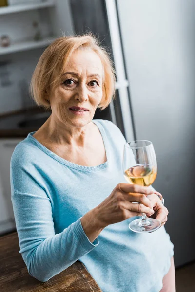 Foyer sélectif de la femme âgée regardant la caméra et tenant verre à vin à la maison — Photo de stock