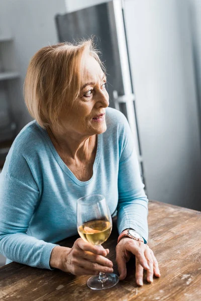 Selektiver Fokus der Seniorin, die wegschaut und zu Hause ein Weinglas hält — Stockfoto