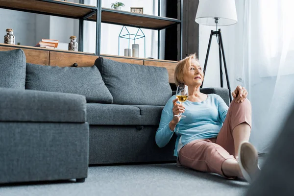 Mulher sênior sentado e segurando copo de vinho na sala de estar com espaço de cópia — Fotografia de Stock