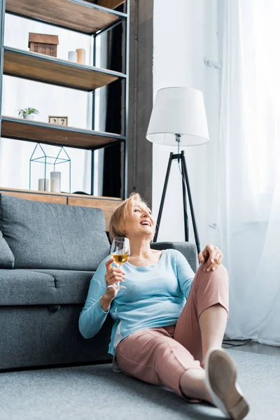 Lachende Seniorin sitzt und hält Weinglas im Wohnzimmer — Stockfoto