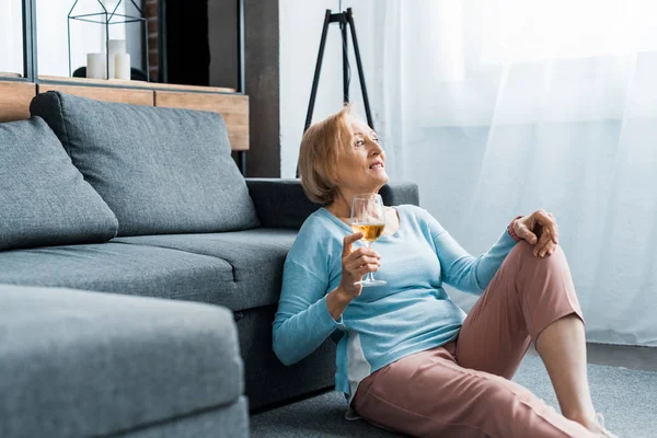 Mujer mayor sentada y sosteniendo copa de vino en la sala de estar con espacio de copia - foto de stock