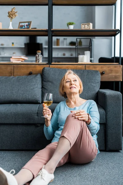Пожилая женщина сидит, глядя в сторону и держа бокал вина в гостиной — стоковое фото