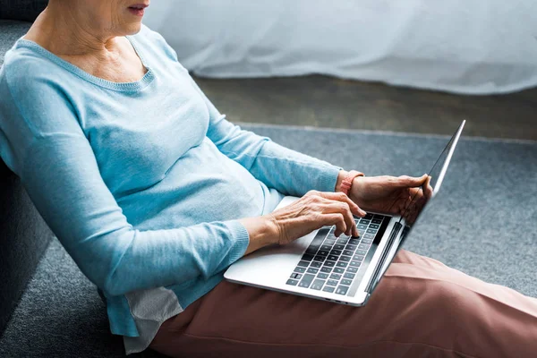 Vista ritagliata della donna anziana digitando sul computer portatile a casa — Foto stock