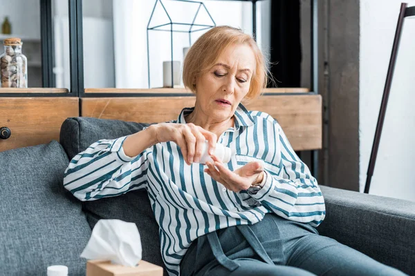 Sick senior woman sitting on couch and taking pills at home — Stock Photo