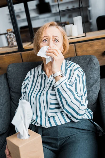 Femme âgée malade avec nez qui coule tenant des tissus et souffrant de froid à la maison — Photo de stock