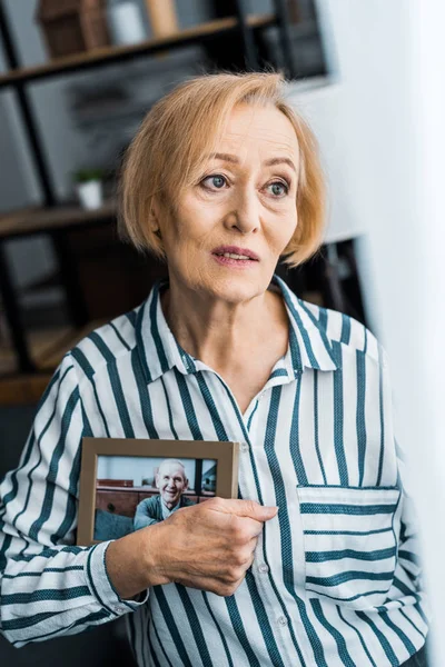 Traurige Seniorin hält Rahmen mit Mann auf Foto zu Hause — Stockfoto