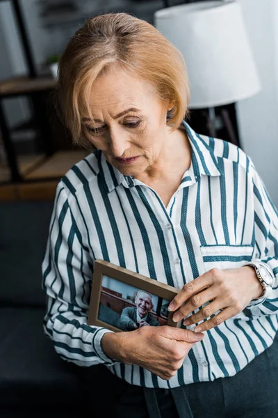 Traurige Seniorin hält Rahmen mit Mann auf Foto zu Hause — Stockfoto